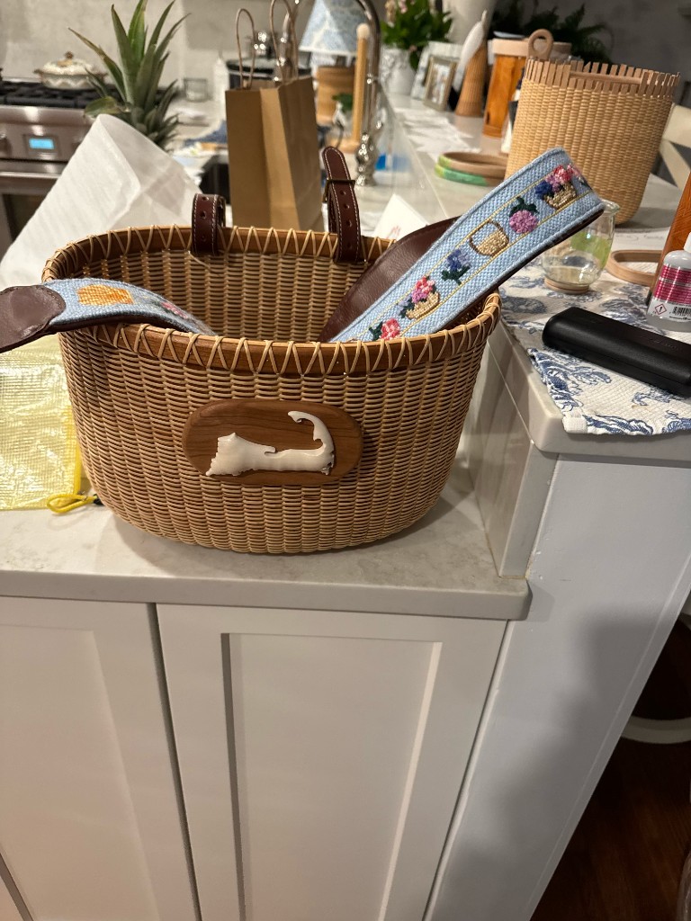 A needlepoint strap stitched with baskets and flowers, on a Nantucket basket