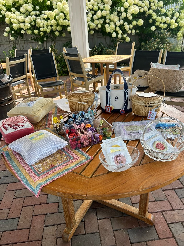 Pillows, baskets, and canvases set out on a table under the hydrangeas